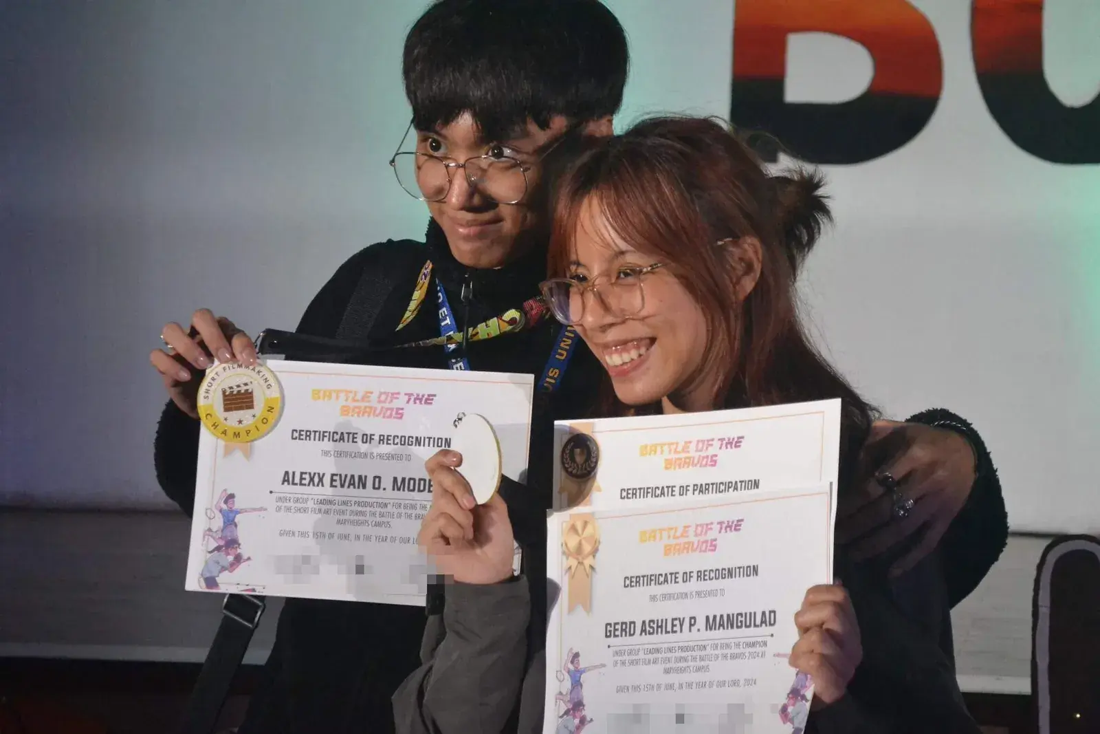 Two team members holding the champion certificates and a short filmmaking medal